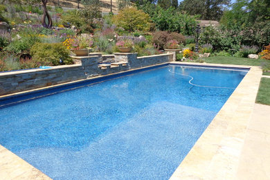 Modelo de piscina grande rectangular en patio trasero con adoquines de piedra natural