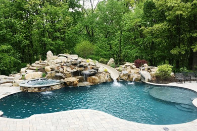 Imagen de piscina con tobogán natural clásica grande a medida en patio trasero con adoquines de ladrillo