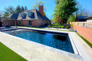 Diseño de piscina con fuente alargada moderna grande rectangular en patio trasero con adoquines de hormigón