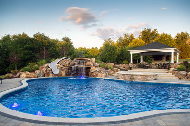 Foto de piscina con tobogán natural grande a medida en patio trasero con adoquines de piedra natural