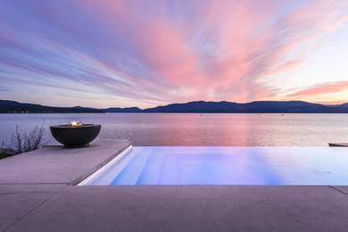 Foto di una grande piscina a sfioro infinito minimalista rettangolare dietro casa con lastre di cemento