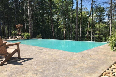 Large trendy backyard concrete and rectangular infinity pool photo in Other