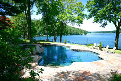Diseño de piscina natural rústica grande a medida en patio trasero con adoquines de piedra natural