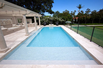 Diseño de piscina alargada mediterránea grande rectangular en patio trasero con adoquines de piedra natural