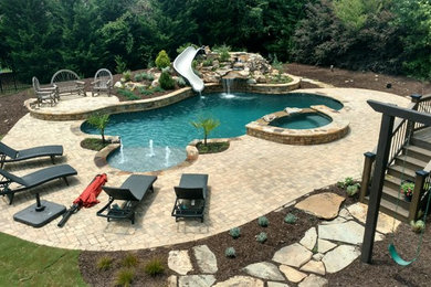 Foto de piscina con tobogán natural grande a medida en patio trasero con adoquines de ladrillo