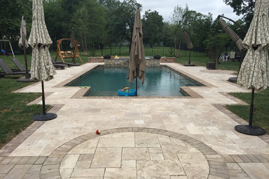 Modelo de piscina moderna grande rectangular en patio trasero con adoquines de piedra natural