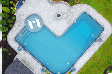 Large backyard concrete paver and l-shaped pool fountain photo in New York