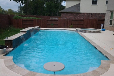 Modelo de piscina con fuente alargada actual grande a medida en patio trasero con losas de hormigón