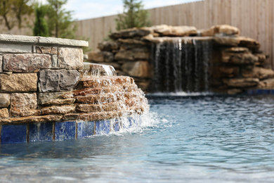 Ejemplo de piscina con fuente alargada de estilo americano grande a medida en patio trasero con losas de hormigón