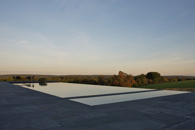 На фото: большой прямоугольный бассейн на заднем дворе в стиле неоклассика (современная классика) с джакузи и покрытием из каменной брусчатки
