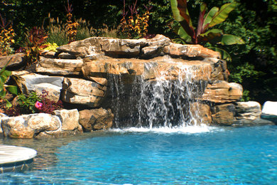 Imagen de piscina con fuente infinita exótica grande a medida en patio trasero con adoquines de piedra natural