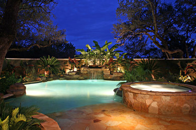 Ispirazione per una piscina naturale tropicale personalizzata di medie dimensioni e dietro casa con pavimentazioni in pietra naturale e una vasca idromassaggio