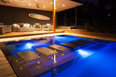 Modelo de piscina contemporánea grande rectangular en patio trasero con adoquines de piedra natural