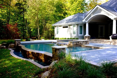 Immagine di una grande piscina a sfioro infinito design personalizzata dietro casa con una vasca idromassaggio e pavimentazioni in pietra naturale