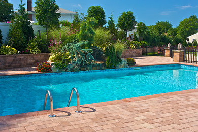 Imagen de piscina clásica de tamaño medio en patio trasero con adoquines de hormigón