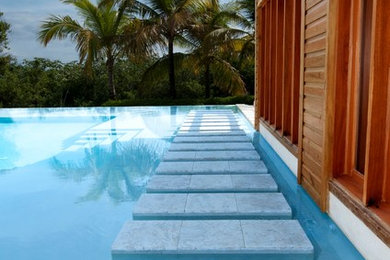 Aménagement d'une piscine à débordement et arrière exotique de taille moyenne et sur mesure avec un point d'eau et des pavés en pierre naturelle.