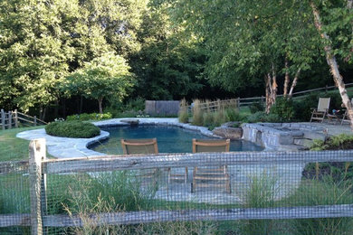 Design ideas for a large rustic back custom shaped hot tub in New York with natural stone paving.