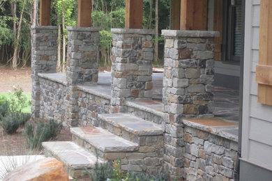 This is an example of a rustic stone front porch design in Other with a roof extension.