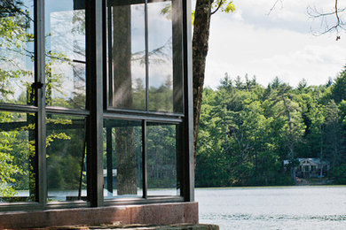 This is an example of an eclectic stone screened-in back porch design in Boston with a roof extension.