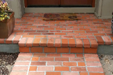 This is an example of a small brick front porch design in Kansas City with a roof extension.