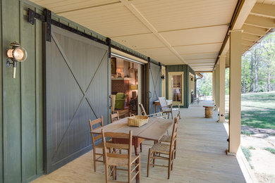 Foto på en stor lantlig veranda framför huset, med trädäck och takförlängning