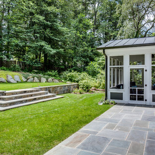 Immagine di un grande portico stile americano dietro casa con un portico chiuso, pavimentazioni in pietra naturale e un tetto a sbalzo