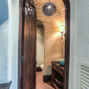 Foto di un piccolo bagno di servizio mediterraneo con ante lisce, ante in legno bruno, WC a due pezzi, pareti beige, pavimento in terracotta, lavabo a bacinella, top in legno e pavimento rosso