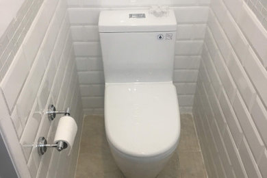 Example of a small white tile and subway tile porcelain tile and beige floor powder room design in Toronto with recessed-panel cabinets, white cabinets, a one-piece toilet, white walls, an integrated sink, glass countertops, green countertops and a freestanding vanity