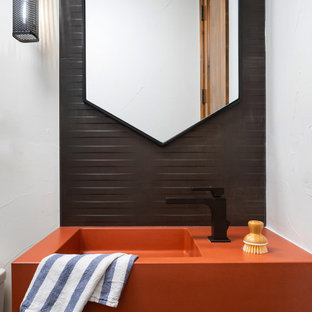 Bild på ett litet funkis orange oranget badrum, med orange skåp, en toalettstol med hel cisternkåpa, svart kakel, keramikplattor, vita väggar, klinkergolv i keramik, ett konsol handfat, bänkskiva i betong och grått golv