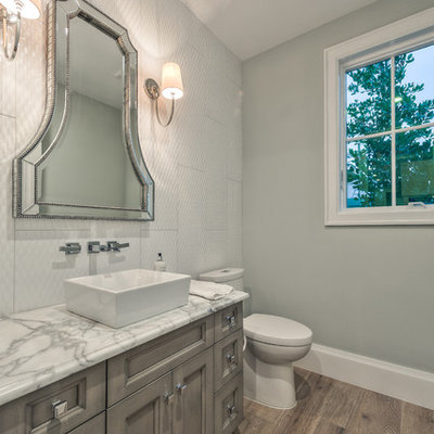 Small gray tile and cement tile light wood floor and brown floor powder room photo with recessed-panel cabinets, gray cabinets, a two-piece toilet, gray walls, a vessel sink and granite countertops