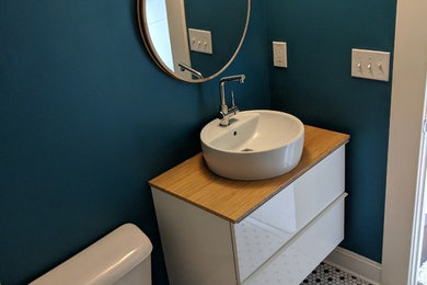 Mid-sized mid-century modern mosaic tile floor and multicolored floor powder room photo in Atlanta with flat-panel cabinets, white cabinets, a two-piece toilet, blue walls, a vessel sink, wood countertops and brown countertops