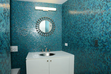 Idée de décoration pour un petit WC et toilettes design avec un placard à porte plane, des portes de placard blanches, un carrelage bleu, mosaïque, un mur multicolore, un lavabo encastré, un plan de toilette en quartz modifié et un plan de toilette blanc.