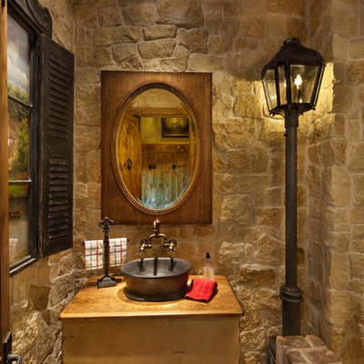 Example of a mid-sized tuscan beige tile and stone tile brick floor and beige floor powder room design in Dallas with open cabinets, a vessel sink, wood countertops, light wood cabinets, a two-piece toilet, beige walls and brown countertops