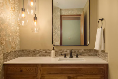 Small transitional multicolored tile and glass tile medium tone wood floor and brown floor powder room photo in Seattle with raised-panel cabinets, brown cabinets, a wall-mount toilet, beige walls, an undermount sink, quartz countertops and white countertops