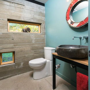 Photo of a small industrial powder room in Philadelphia with a two-piece toilet, blue walls, concrete floors, a vessel sink, black cabinets, wood benchtops, beige floor and brown benchtops.