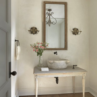 Cette image montre un WC et toilettes style shabby chic avec un placard en trompe-l'oeil, des portes de placard en bois vieilli, un mur beige, un sol en bois brun, une vasque et un sol marron.