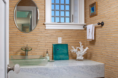 ポートランド(メイン)にある高級な小さなビーチスタイルのおしゃれなトイレ・洗面所 (オープンシェルフ、ベージュのタイル、ベージュの壁、濃色無垢フローリング、ベッセル式洗面器、珪岩の洗面台、グレーの床) の写真