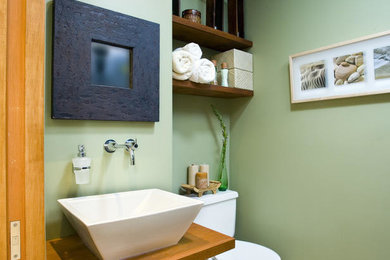 Ejemplo de aseo actual pequeño con sanitario de dos piezas, paredes verdes, lavabo sobreencimera, encimera de madera y encimeras marrones