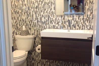 Example of a mid-sized trendy porcelain tile powder room design in Orange County with flat-panel cabinets, dark wood cabinets, a two-piece toilet, multicolored walls, an integrated sink and solid surface countertops