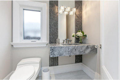 Powder room - mid-sized contemporary gray tile and stone tile ceramic tile and white floor powder room idea in Toronto with a wall-mount toilet, gray walls, an integrated sink, marble countertops and gray countertops