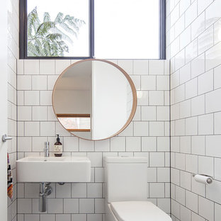 Photo of a midcentury powder room in Melbourne with white tile, white walls, mosaic tile floors, a wall-mount sink and black floor.
