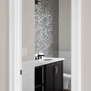 Ispirazione per un bagno di servizio tradizionale di medie dimensioni con ante con riquadro incassato, ante nere, WC sospeso, piastrelle grigie, piastrelle in metallo, pareti grigie, lavabo sottopiano, pavimento marrone, top bianco, mobile bagno incassato, soffitto a volta e pavimento in legno massello medio