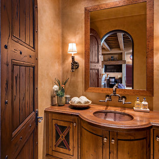 Aménagement d'un WC et toilettes sud-ouest américain avec un placard en trompe-l'oeil, un WC à poser, un sol en calcaire, un lavabo encastré et un plan de toilette en bois.