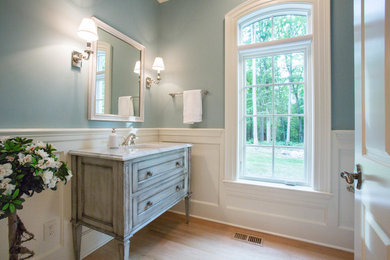 Klassisk inredning av ett mellanstort toalett, med möbel-liknande, skåp i slitet trä, blå väggar, ljust trägolv, ett undermonterad handfat och marmorbänkskiva