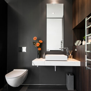 Idée de décoration pour un WC et toilettes design de taille moyenne avec une vasque, des portes de placard en bois sombre, un plan de toilette en marbre, un WC suspendu, un mur noir et un sol en carrelage de céramique.