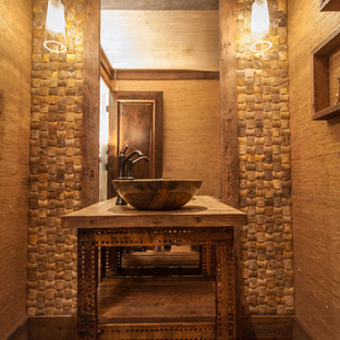 Foto di un piccolo bagno di servizio tropicale con lavabo a bacinella, nessun'anta, ante con finitura invecchiata, top in legno, WC a due pezzi, piastrelle beige, piastrelle in pietra, pareti beige, pavimento in legno massello medio e top marrone