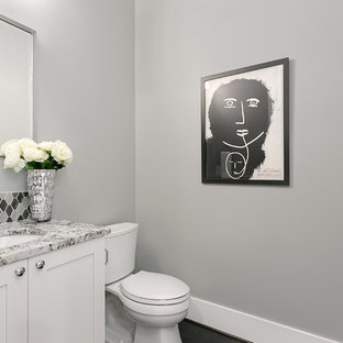 Aménagement d'un petit WC et toilettes craftsman avec un placard à porte shaker, un WC séparé, un carrelage gris, des carreaux de porcelaine, un sol en carrelage de porcelaine, un lavabo encastré, des portes de placard blanches, un mur gris et un plan de toilette en granite.