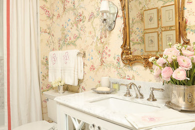 Inredning av ett klassiskt litet toalett, med luckor med glaspanel, vita skåp, en toalettstol med separat cisternkåpa, vit kakel, rosa väggar, marmorgolv, ett undermonterad handfat och marmorbänkskiva