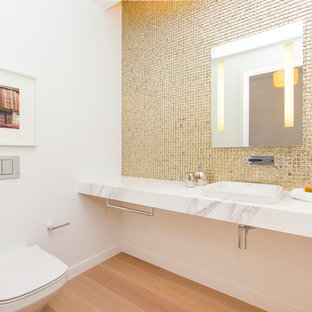 Exemple d'un WC et toilettes tendance de taille moyenne avec un WC suspendu, un mur blanc, un sol en bois clair, un lavabo posé, un plan de toilette en marbre, carrelage en métal et un sol beige.
