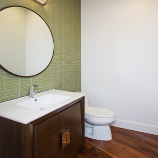 Kleine Retro Gästetoilette mit flächenbündigen Schrankfronten, dunklen Holzschränken, Toilette mit Aufsatzspülkasten, grünen Fliesen, Glasfliesen, weißer Wandfarbe, dunklem Holzboden, integriertem Waschbecken, Quarzwerkstein-Waschtisch und braunem Boden in Dallas